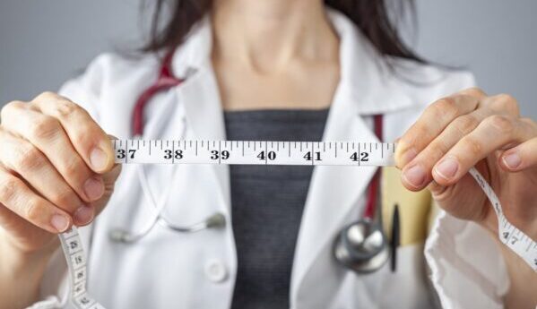 Close up isolated image of a caucasian doctor holding a tape measure in her hands which shows 40 inches as abdominal circumference upper limit in healthy people. Concept for weigh loss and fitness.